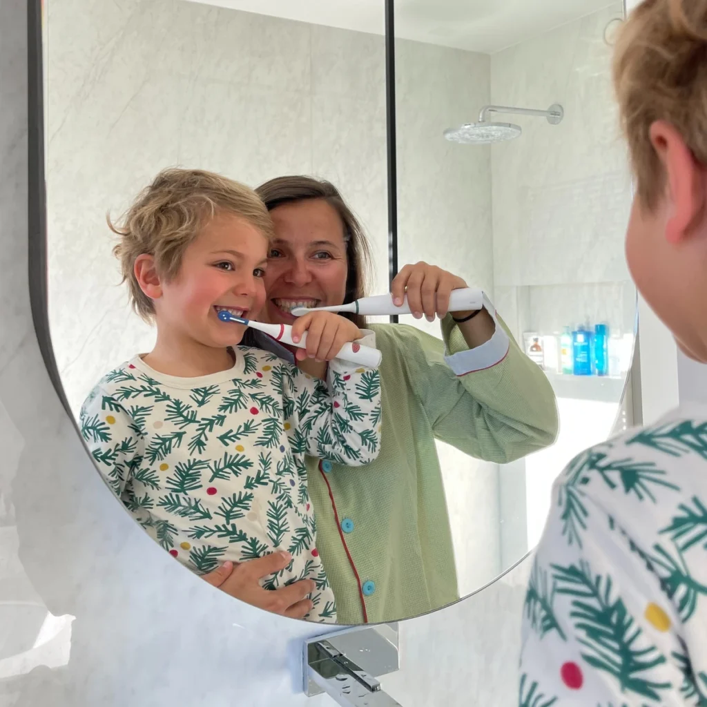 madre y niño lavándose los dientes frente al espejo con el cepillo de dientes eléctrico infantil