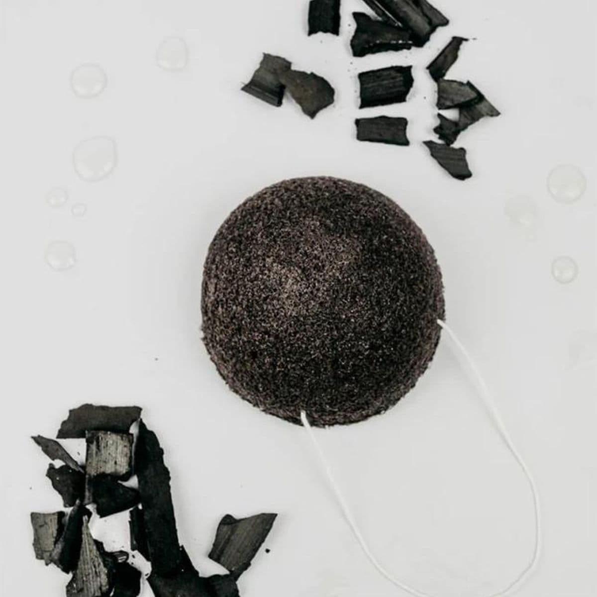 esponja facial de konjac negra de banbu rodeada de trozos de carbón