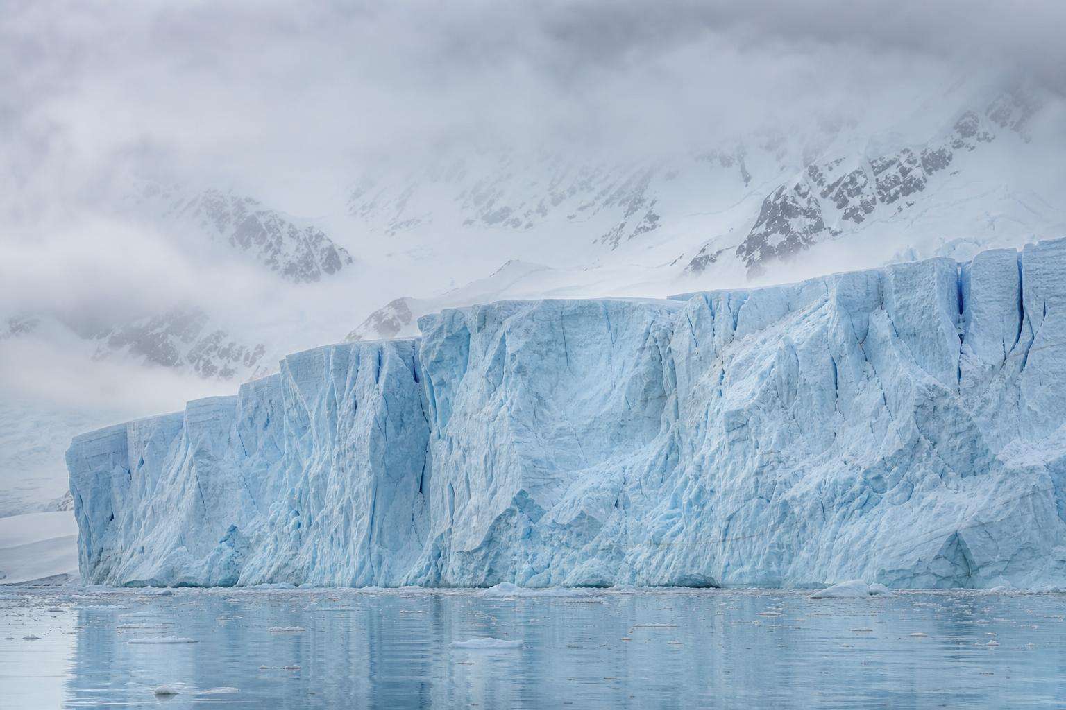 Frente de un glaciar de hielo azulado sobre un mar en calma en la Antártida, bajo luz fría