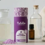 Bote de cristal con suavizante casero de vinagre y aceite esencial de lavanda sobre superficie de madera clara con flores secas de lavanda