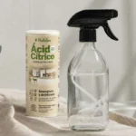 Ácido cítrico en polvo y botella de vidrio con pulverizador sobre encimera de baño para quitar la cal de los grifos
