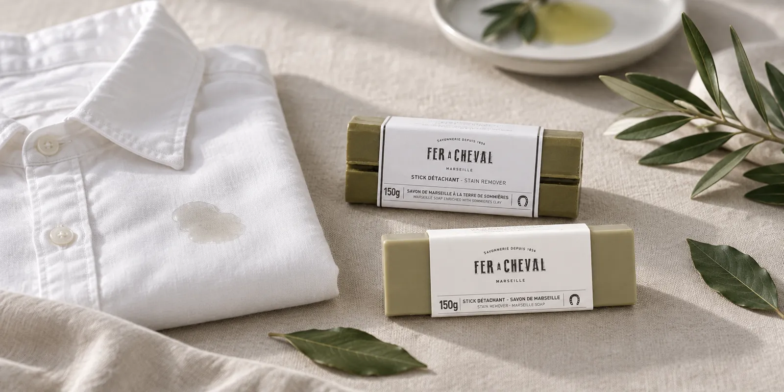 Camisa blanca con una mancha de aceite junto a dos pastillas de jabón quitamanchas sobre lino crudo