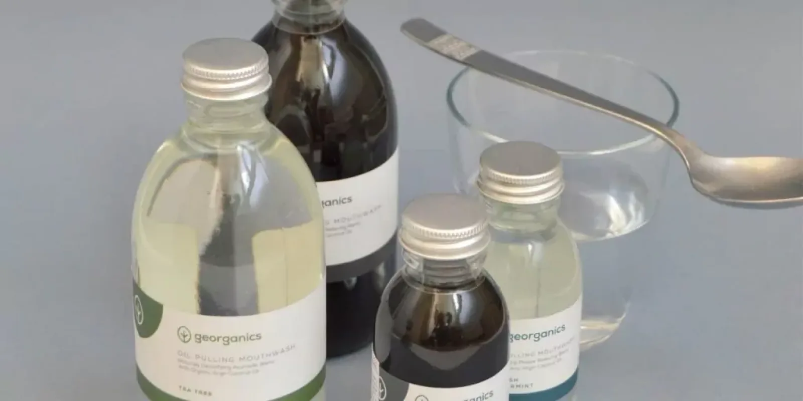 Botellas de cristal con tapón metálico de enjuague bucal líquido junto a un vaso de agua y una cuchara