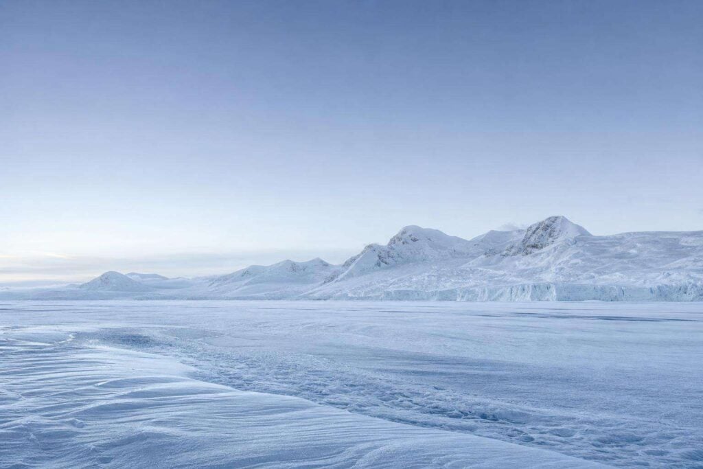 Paisaje de la Antártida: extenso campo de hielo y nieve prístina bajo luz fría, con montañas nevadas al fondo