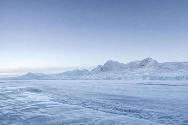 Paisaje de la Antártida: extenso campo de hielo y nieve prístina bajo luz fría, con montañas nevadas al fondo