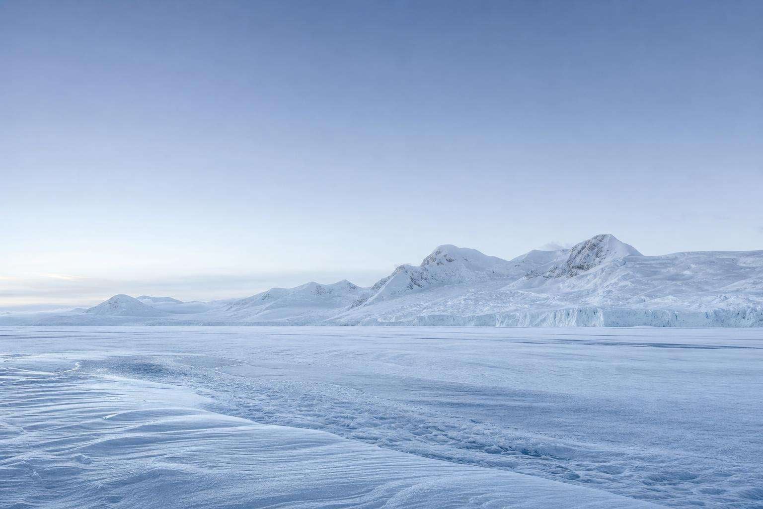 Paisaje de la Antártida: extenso campo de hielo y nieve prístina bajo luz fría, con montañas nevadas al fondo