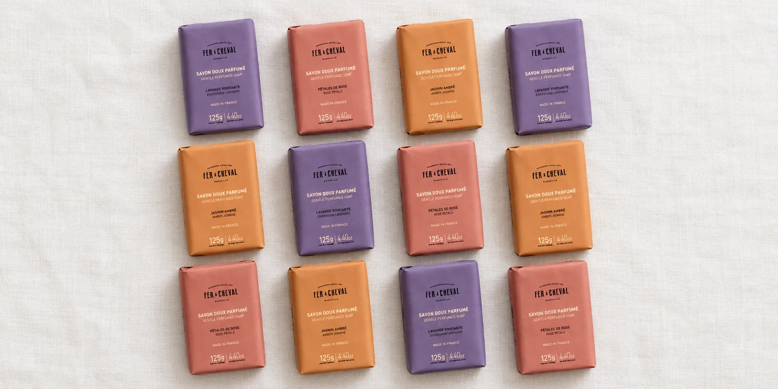 Pastillas de jabón perfumado Fer à Cheval con su envoltorio nuevo de papel de color, en filas sobre lino blanco